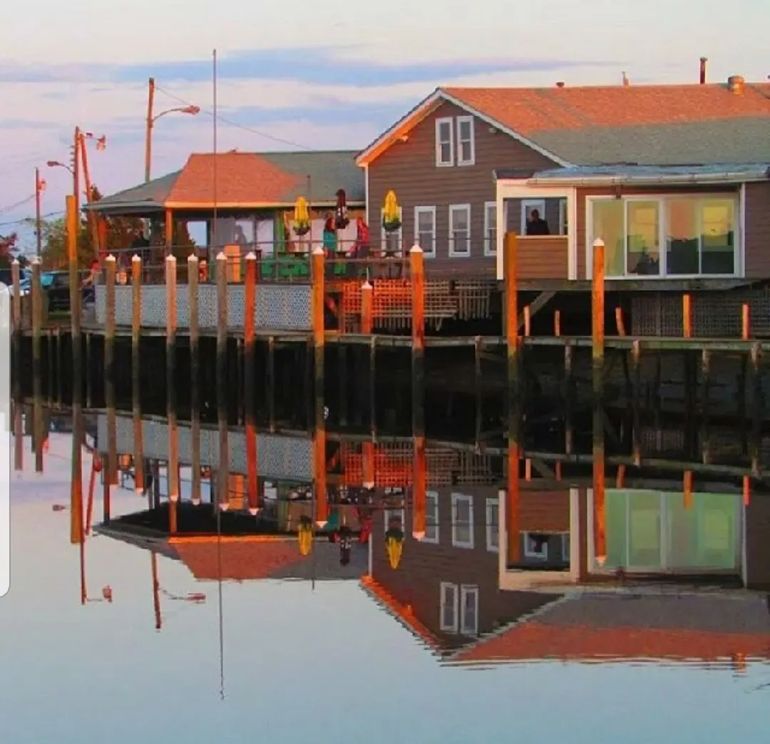 Oyster Creek's restaurant and boat bar reflected in the still creek, with tables along the waterfront
